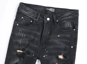 Dettaglio in denim nero invecchiato con toppe in rete colorata e schizzi di vernice