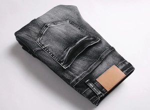 Detail of dark grey washed denim jeans with vintage faded texture and brown leather patch