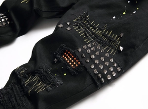 Detailed close-up of distressed black denim with silver studs and orange patchwork accents