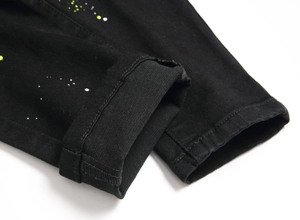 Detail of black denim fabric featuring artistic white and neon yellow paint splatter effects