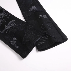 Gros plan d'un jean flare noir avec broderies en zigzag et détails déchirés de style urbain