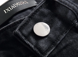 Dettaglio macro della vita in denim nero con bottone argento e patch di marca in pelle