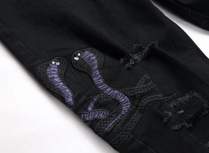 Detail der Cobra Stickerei und Distressed-Risse auf schwarzen Stretch-Streetwear-Jeans