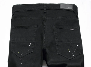 Macro view of black denim jeans featuring white paint splatter and leather waist tag