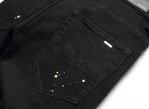 Detail of black men's denim jeans with white paint splatter and metal studs on back pocket