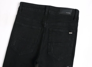 Detailaufnahme der schwarzen Jeans mit Leder-Markenlabel und Logo aus Metall am Bund