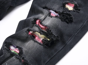Dettaglio macro di jeans neri strappati con applicazioni di strass colorati sugli strappi