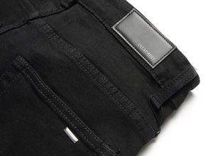 Detail of black denim jeans with leather logo patch and metallic rivet accents