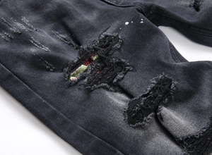 Dettaglio di jeans neri invecchiati con toppe in tessuto colorato all'interno degli strappi