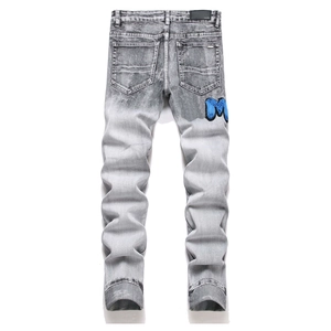 Detail view of grey denim pants featuring a leather brand patch and blue embroidered M logo