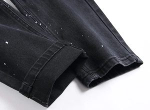 Dettaglio dell'orlo dei jeans neri con schizzi di vernice bianca e trama in twill