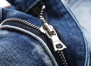 Detailansicht des Metallreißverschlusses und der orangefarbenen Nähte an blauen Denim-Jeans