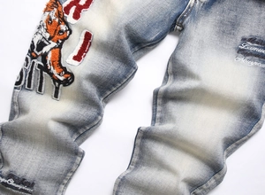 Close-up of vintage blue jeans with tiger head embroidery and distressed fringe hem detail