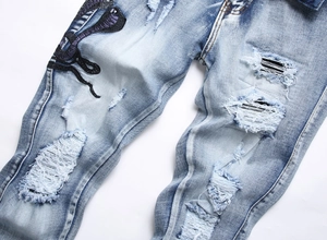 Detailansicht der Schlangenstickerei und Riss-Effekte an der hellblauen Denim-Jeanshose