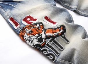 Detail of tiger head embroidery and textured patches on light blue washed denim jeans