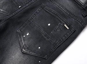 Dettaglio dei jeans neri con macchie di vernice bianca e logo in metallo sulla tasca posteriore