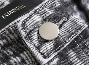 Macro view of grey distressed denim waist featuring a silver button and detailed stitching