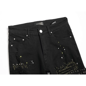Men's slim black ripped denim jeans with yellow paint splatter and metal rivet details
