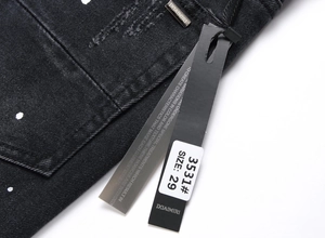 Dettaglio di jeans neri strappati con targhetta in metallo e etichetta della taglia in vita