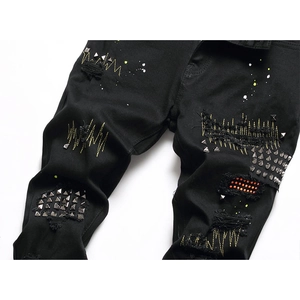 Men's black distressed denim jeans with embroidery, metal rivets and paint splatter details
