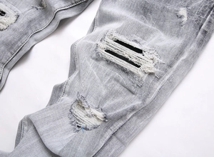 Detailed close-up of frayed denim distressing and patch embroidery on grey street jeans