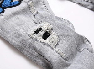 Detailed view of grey distressed jeans featuring blue embroidery and patchwork accents