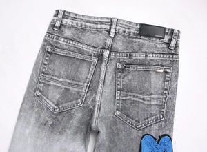Detail of grey washed denim jeans with blue embroidered patch and leather back tag