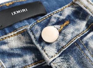 Detail of blue wash denim waist featuring silver metal button and IXMIRI woven brand label