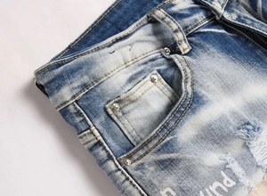 Detail of blue high-street jeans featuring distressed texture, cat whisker fading and rivets