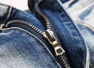 Detailed close-up of high-quality metal zipper and stitching on blue washed denim jeans