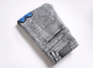 Detailed view of blue rose floral embroidery and acid wash texture on grey denim jeans