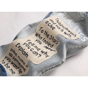 Detail of light blue washed denim with distressed patches and printed street style slogans