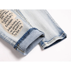 Close-up of light blue washed denim pants featuring a trendy letter patch and cuffed hem