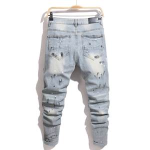 Detail of distressed light blue slim jeans with multi-color paint splatters and leather patch