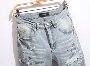 Detailed view of heavy washed blue jeans with paint splatters and woven knee patches