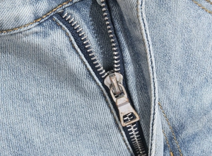 Macro shot of high-quality silver metal zipper on light blue distressed denim pants