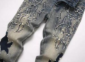 Vue détaillée du jean bleu délavé avec broderie de flammes et ornements de perles nacrées
