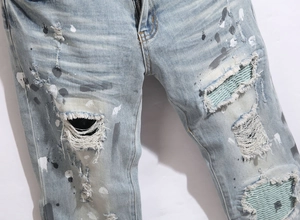 Close-up detail of distressed blue skinny jeans with paint splatters and ripped knees