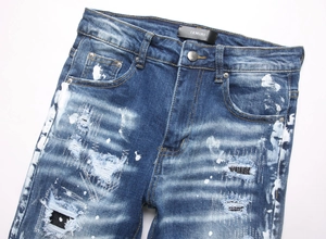 Detailed close-up of blue distressed denim with white paint splatters and ripped accents