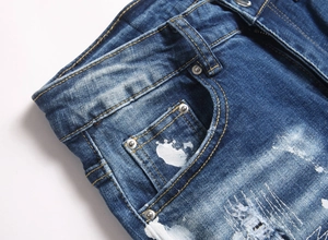 Detail view of blue distressed denim jeans with paint splatters and ripped textures