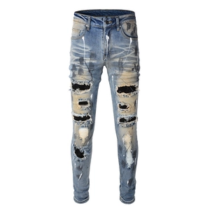 Distressed slim fit jeans with paint splatter and ripped patches in light blue denim