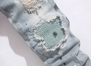 Detail of distressed light blue denim jeans with green pleated patch and paint splatters