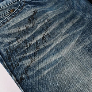 Detail of vintage washed blue denim with hand-drawn graffiti text and metal rivets
