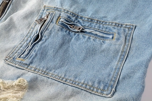 Detail of distressed light blue denim jacket featuring double zippers and ripped texture
