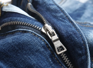 Detail of silver metal zipper and yellow contrast stitching on blue denim jeans
