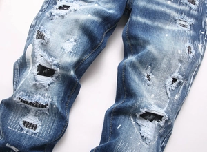 Detail of distressed blue jeans with white paint splatters and black patches
