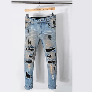 Detail of distressed light blue slim jeans with paint splatters and black sequin patches