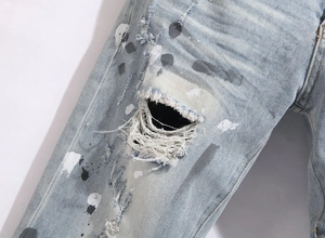 Detail shot of blue distressed jeans featuring ripped holes and paint splatter effects