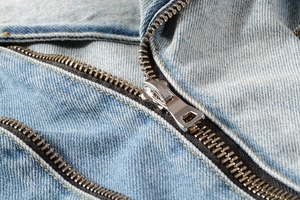 Detailed macro shot of silver metal zipper and yellow stitching on blue denim jacket