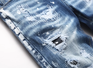 Detailed close-up of blue distressed denim jeans with white paint splatters and ripped edges